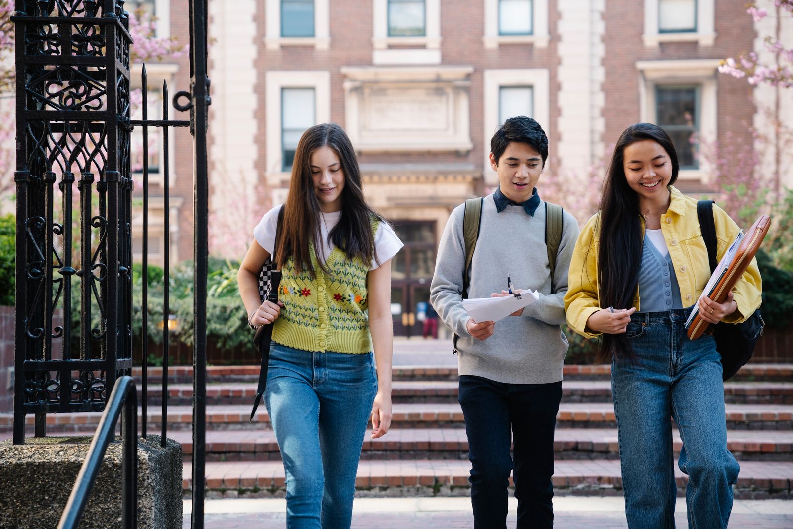 Three university students walking together on campus with notebooks and backpacks